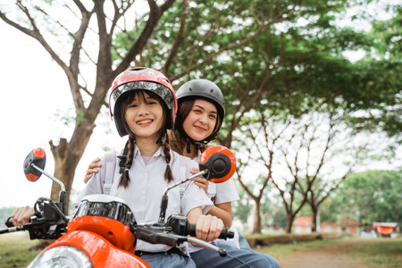 Two beautiful high school students wearing helmets smiling for the camera while riding a motorcycle on the roadの写真素材