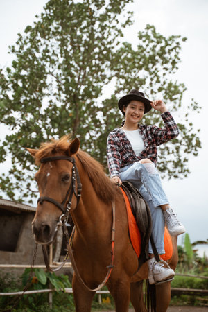 beautiful cowboy girl smiling sitting on horse on outdoor backgroundの写真素材