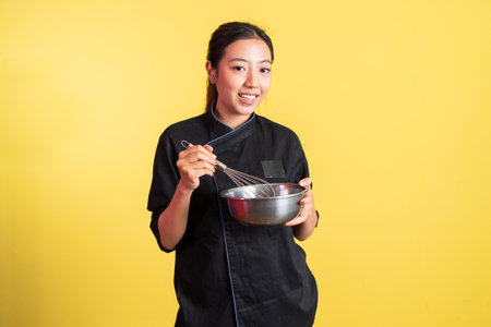 Asian female chef carrying stainless basin and holding whisk on isolated backgroundの写真素材