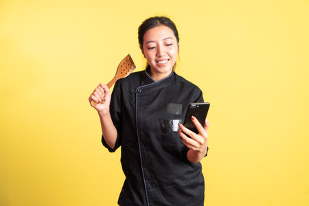 asian female chef using mobile phone and holding spatula on isolated backgroundの写真素材
