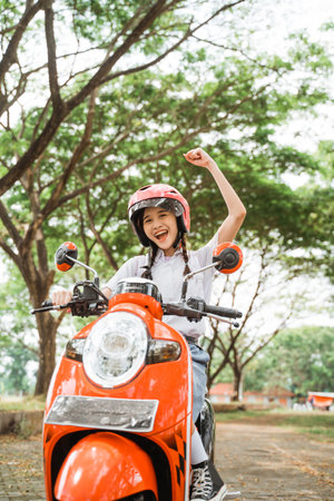 student girl is excited to celebrate by riding a motorcycle wearing a helmet on the roadの写真素材