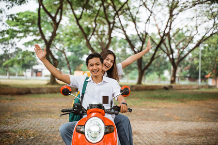 Couple of high school students waving riding motorbike on the streetの写真素材