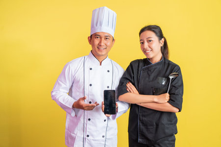 male chef showing blank mobile phone screen with female chef with hands crossed on isolated...