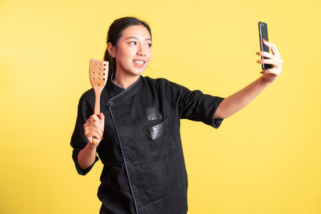 female chef selfie using mobile phone and hand holding spatula on isolated backgroundの写真素材