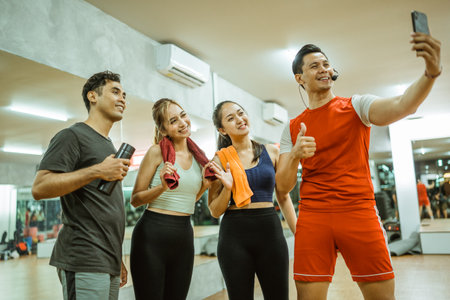 asian male instructor and young sporty group selfie together with smartphone camera in fitness centerの写真素材