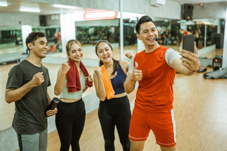 Men and women with coach selfie together with cellphone camera in fitness centerの写真素材