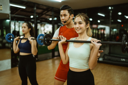 male instructor accompanies a young sporty group during a barbell lifting exercise in a fitness centerの写真素材