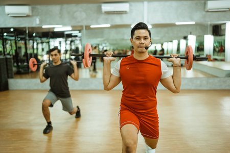 male instructor doing back squats with a barbell during a group workout at the fitness centerの写真素材