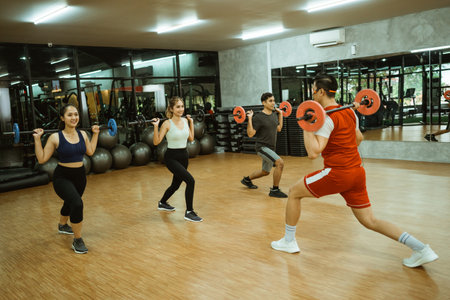 male instructor gives an example of back squats with a barbell in front with a young sporty group in the fitness centerの写真素材