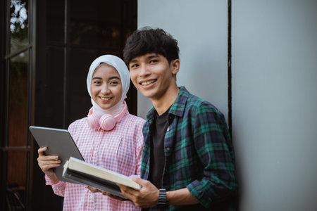 Muslim girl with a pad and a boy with a book smiling at the camera while standing side by side