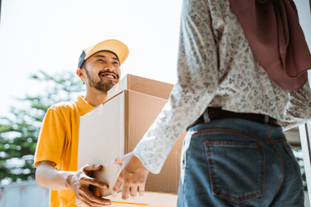 delivery man in yellow uniform smiling friendly while delivering package boxes to customersの写真素材