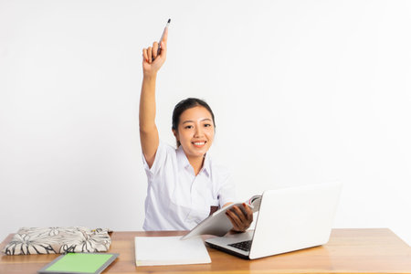 high school girl at desk holding book with pointing finger while using laptop on isolated background