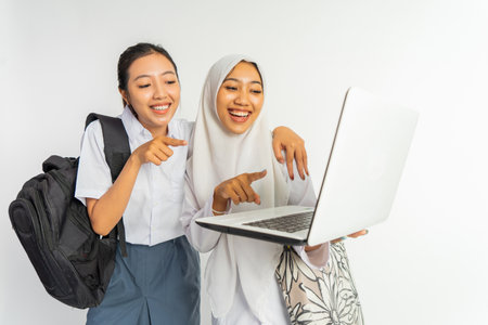 two smiling vocational high school girls carrying bags while using a laptop on a white backgroundの写真素材