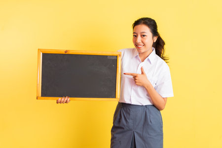 girl in high school uniform holding blackboard beside her with finger pointing on isolated backgroundの写真素材