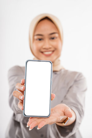a beautiful woman with hijab standing and showing the phone at her hand with a white backgroundの写真素材