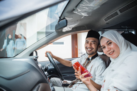 Asian Muslim couple smiles while using cell phone in car when going to their friends houseの写真素材