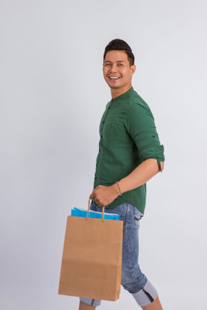 asian man smiling while walking and bring the shopping bags on isolated background
