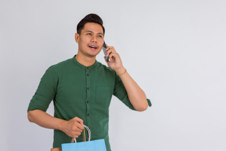 asian man calling someone on phone while bring the shopping bags on isolated backgroundの写真素材