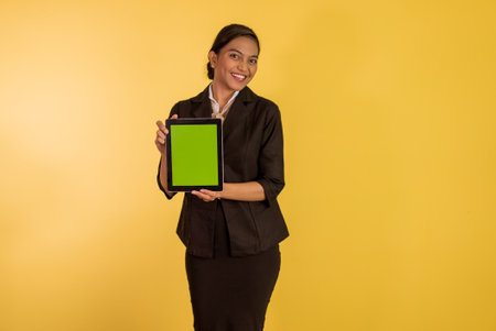 asian woman in formal outfit showing the digital tablet with green screen on orange isolated backgroundの写真素材