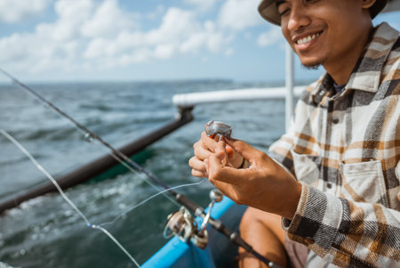 Asian angler puts bait on a hook while casting with a small fishing boat at sea