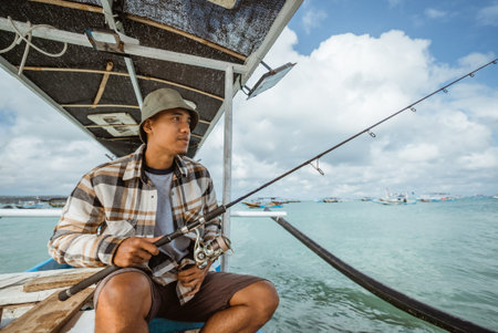 Asian anglers sit with their fishing rods as they set out to fish in a small boatの写真素材