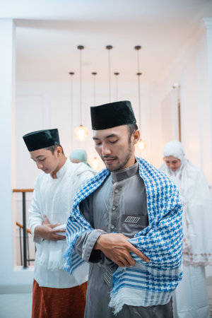 Asian men in caps perform iftitah prayer movements during congregational prayers