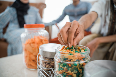 guests hand takes a snack from a glass jar full of snacks on the table in the living roomの写真素材