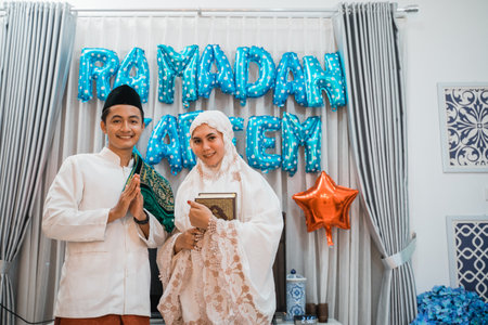 asian muslim couple wishes happy ramadan with hand gesture at homeの写真素材
