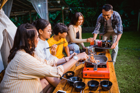 woman in orange stripped shirt taking the grilled beef from the grilled pan while the guy in plaid shirt put the drinks on the tableの写真素材
