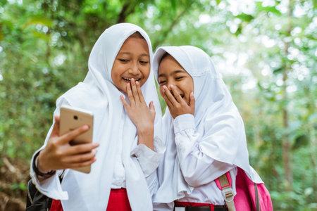 two male elementary students in uniform standing together at the side of the country road watching...