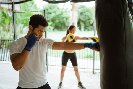the male and female boxer hitting the sand bag. boxing coach with partner in the gym trainingの写真素材