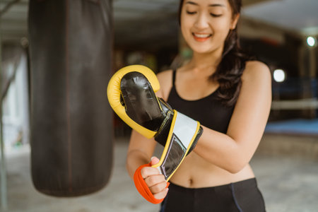 a female boxer standing with the hand wraps at her right hand while wearing the boxing gloves at her left hand inside the boxing studioの写真素材