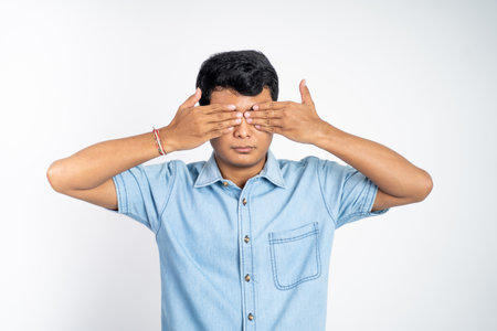 portrait of young Asian man standing with two eyes closed against an isolated backgroundの写真素材