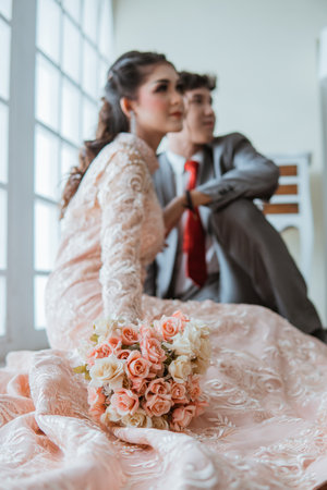 asian bride holding the flowers bouquet while sitting on the floor beside the groomの写真素材