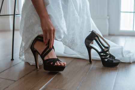 the hand of the bride in white gown wearing the black heels while sitting on a chairの写真素材