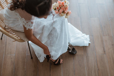 asian bride in white gown bring the flowers bouquet while wearing the black heels and sitting on the chairの写真素材