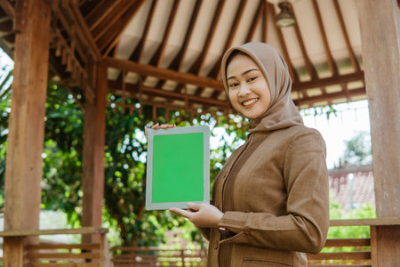 young female teacher in headscarf showing screen a pad with gazebo in the backgroundの写真素材