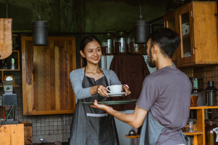 beautiful barista in apron put the cup of coffee on the tray that holded by the waiter outside the bar deskの写真素材