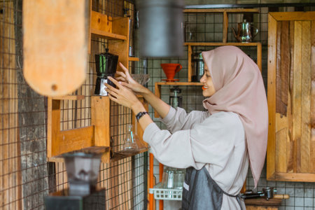 female barista with hijab in apron take the dripper from the organizer inside the bar deskの写真素材