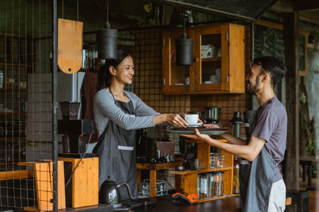 female barista put the cup of coffee on the tray that holded by the waiter outside the bar deskの写真素材