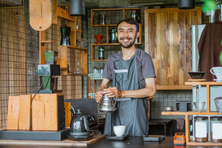 male barista in apron standing with smile while brewing the coffee inside the bar deskの写真素材