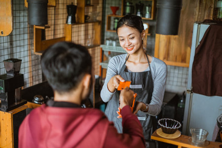 a beautiful barista receiving the credit card from the customer during the transaction on the cashier deskの写真素材
