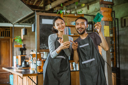 male barista raising the deposit book while pointing on the phone that holded by the female baristaの写真素材