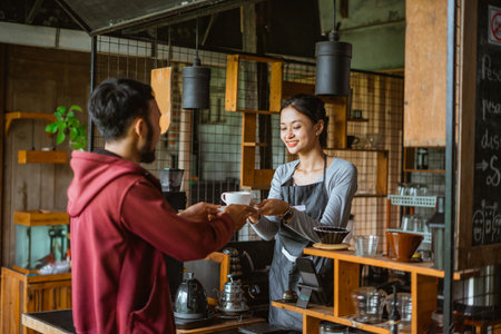 the male customer receiving the cup of coffee from the female barista that standing inside the bar deskの写真素材