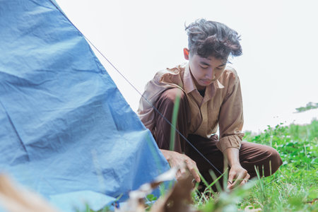 a teenage boy wearing scout clothes set up tent pegs while in the fieldの写真素材