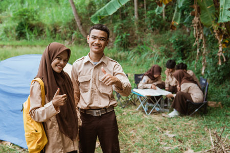 boy scouts and girl scouts carrying backpacks with thumbs up against the background of tents and scout camping backgroundの写真素材