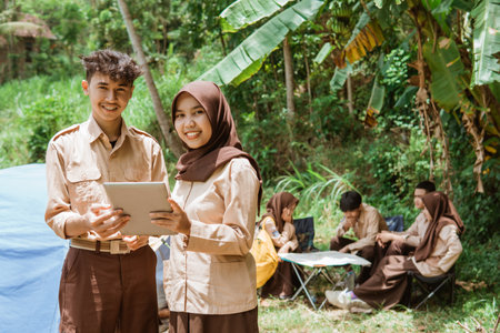 boy scouts and girl scouts smiling while using a digital tablet with scout camping backgroundの写真素材