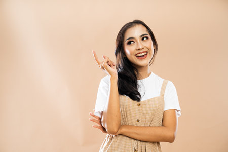 asian woman in casual clothes standing with smile while looking and pointing up on isolated backgroundの写真素材
