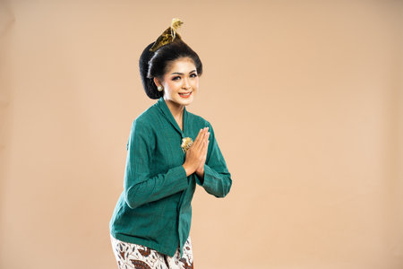 beautiful asian woman in green kebaya standing bent over with hands put together on isolated backgroundの写真素材