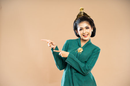 javanese woman in green kebaya standing with smile and pointing with her fingers on isolated backgroundの写真素材